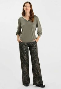 Olivgrünes Oberteil mit V-Ausschnitt und dreiviertellangen Ärmeln, kombiniert mit dunkel gemusterten, weit geschnittenen Leopardenhose. Glatte Stofftextur, minimalistische Akzente.