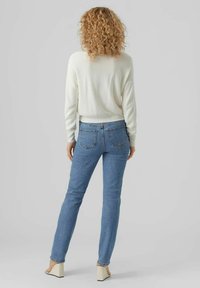 Pull blanc léger côtelé, jeans droits bleu, et sandales à talons carrés beige, vus de dos. Les jeans possèdent des poches arrières.