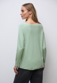 Mintgrüner Langarmpullover mit lockerer Passform, weitem Ausschnitt und weichem Material, kombiniert mit dunkelgrauen Hosen.