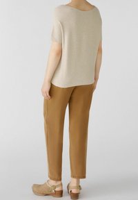 Haut beige à manches courtes avec une coupe décontractée, associé à un pantalon marron fuselé. Les chaussures sont des sabots marron clair avec une bride arrière et un talon en bois.