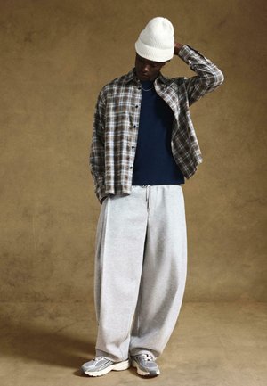 Cămașă din flanel ușoară, cu carouri, în nuanțe de maro și albastru, peste un tricou bleumarin. Pantaloni sport gri, lejeri, și o căciulă albă din tricot. Încălțăminte sport gri.