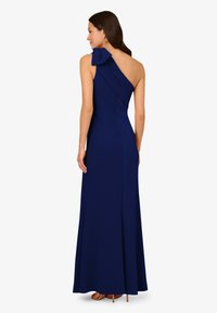 Námořnická modrá, jedno rameno oděv s akcentem mašle, dlouhý střih, přiléhavý korzet a hladká textura. Boční rozparek na lemu.