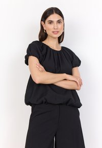 Svart blus med korta puffärmar, rynkad halslinning och lös passform, tillverkad av lätt material. Kombinerad med svarta vida byxor.