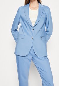 Světle modrá saka vyrobená z hladkého materiálu, s jedním knoflíkem a dvěma knoflíky, jednou náprsní kapsou a dvěma postranními kapsami.