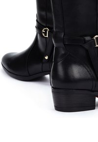 Botas de tobillo de cuero negro con una textura suave, punta redondeada, detalles decorativos de correa y hebilla, y un tacón bajo en bloque.