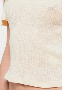 Ανοιχτό μπεζ ριμπ πλεκτό τοπ με κοντά μανίκια, εφαρμοστή γραμμή και ελαφρώς cropped τελείωμα. Το ύφασμα φαίνεται μαλακό και διαπνέον.