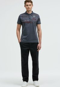Gray polo shirt with graphic text prints, three buttons, and contrasting collar. Paired with black pants and white sneakers.
