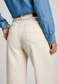 Pantalones de mezclilla de color claro y con rayas, con bolsillos traseros, combinados con una camisa de chambray azul. Presenta un diseño de cintura alta y pierna recta.