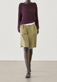 Burgundy, löst gestrickter Pullover kombiniert mit olivgrünen, hochgeschnittenen Shorts; das Modell trägt schwarze Sandalen; glatte Textur, entspannter Schnitt.