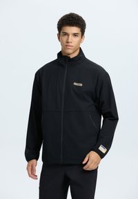 Black zip-up jacket with a high collar, featuring a front pocket and logo detail on the left chest and cuff. Smooth fabric with a relaxed fit.