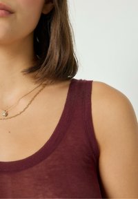 Bordeaux linne med rundad halsringning, mjuk stickad textur och tunna axelband. Guld lagerhalsband med hängen.