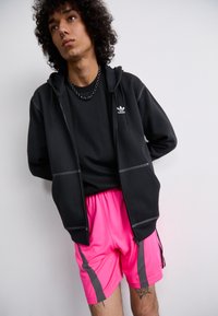 Sort zip-up hættejakke med grå syninger, båret over en sort t-shirt og lyserøde shorts med grå sidelæg.