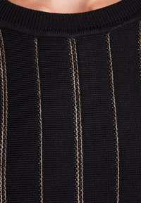 Gros plan sur un pull noir côtelé avec des rayures verticales beiges cousues et un col arrondi sur le cou et la poitrine d'une personne.