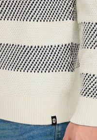 Knitted sweater in cream with navy diagonal stripes; ribbed cuffs and hem; small black logo tag on the lower left side.
