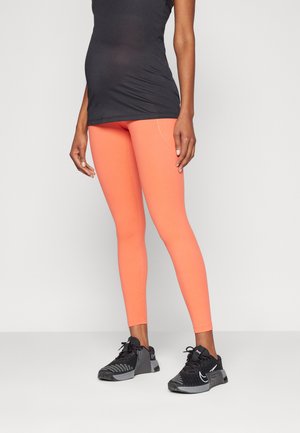 Coral leggings made of stretchy material, featuring a slim fit and seam detailing, paired with a black tank top and athletic shoes.