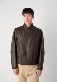 Barna bőrkabát magas gallérral, cipzáras záródással, oldalzsebekkel és varrott részletekkel. Slim fit fazon, sima textúra.