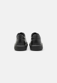 Sneakers in pelle nera con punta arrotondata, texture liscia, suola in gomma a contrasto e minimal branding sul tallone.
