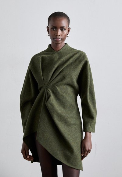 Robe enveloppante verte en laine texturée, avec un décolleté en V profond, des manches longues et un détail froncé à la taille, créant une silhouette asymétrique.