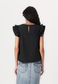 Melnā īsām piedurknēm augšdaļa ar viļņotām piedurknēm, ar spraugām aizmugurē. Kombinēta ar gaiši zilu jeans svārku. Mīksta auduma, brīvs piegriezums.