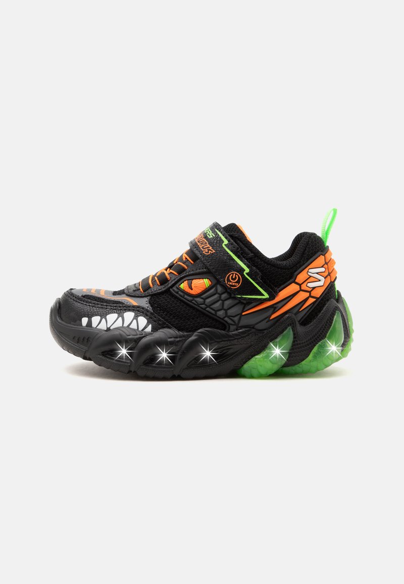 Παιδικό αθλητικό παπούτσι σε μαύρο και πορτοκαλί με σχέδιο ματιού και δοντιών δεινοσαύρου, πράσινη σόλα και φωτιζόμενα στοιχεία στην πλευρά της σόλας.