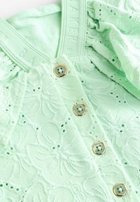 Top verde chiaro con texture, caratterizzato da ricami floreali, bottoni dorati e scollatura a costine con il nome del marchio impresso.