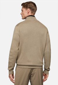 Beige knitted sweater with a textured finish, stand collar, and contrasting black trim at the neckline, displayed from the back.