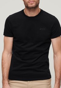 Sort kortærmet t-shirt lavet af bomuld, med rund halsudskæring og et diskret logo på brystet, med en glat tekstur.