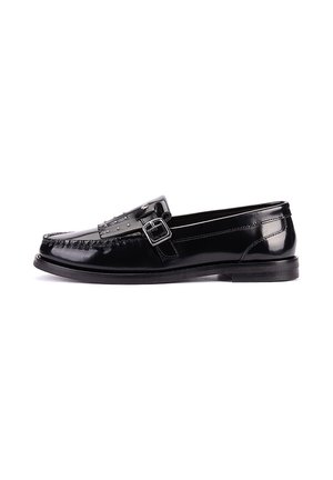 Mocasín negro de cuero brillante con hebilla plateada y detalles de tachuelas en la parte superior, suela plana y diseño frontal cosido.
