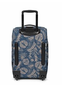 Maleta azul con un patrón de hojas tropicales beige, carcasa dura, asa retráctil y cuatro ruedas negras para una movilidad fácil.