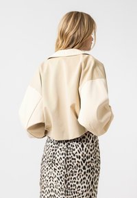 Beige Cropped-Jacke mit übergroßen Ärmeln und einer glatten Textur. Kombiniert mit einem Rock im Leopardenmuster, der ein gepunktetes Muster zeigt.