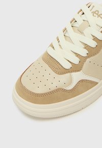 Beige sneakers med glatte lær- og ruskindspaneler, perforert tåboks, tykke snørebånd og gummisåle med teksturert mønster.