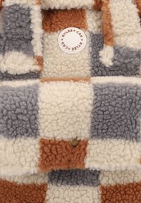 Geweven tote bag met een geblokt patroon in crème, grijs en rustkleur. Gemaakt van zacht, pluizig materiaal met een ronde merketiket.