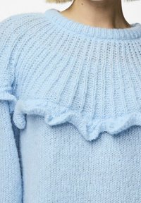 Pull en tricot bleu clair avec un design côtelé, un col rond et un ourlet à volants. Texture douce avec des détails de couture complexes.