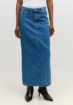 Maxi-Jeansrock in Blau mit einer Knopfleiste an der Vorderseite, zwei Vordertaschen und gerader Silhouette. Getragen mit schwarzen spitzen Absätzen.