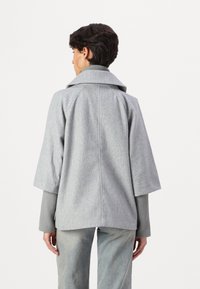 Manteau structuré gris avec des manches larges et courtes et un grand col. Tissu texturé et conception à dos droit. Associé à un haut gris côtelé.