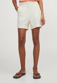 Krämfärgade skräddarsydda shorts med arbetad nederkant, två sidofickor och framveck. Tillverkade av ett slätt tyg med en lätt textur.