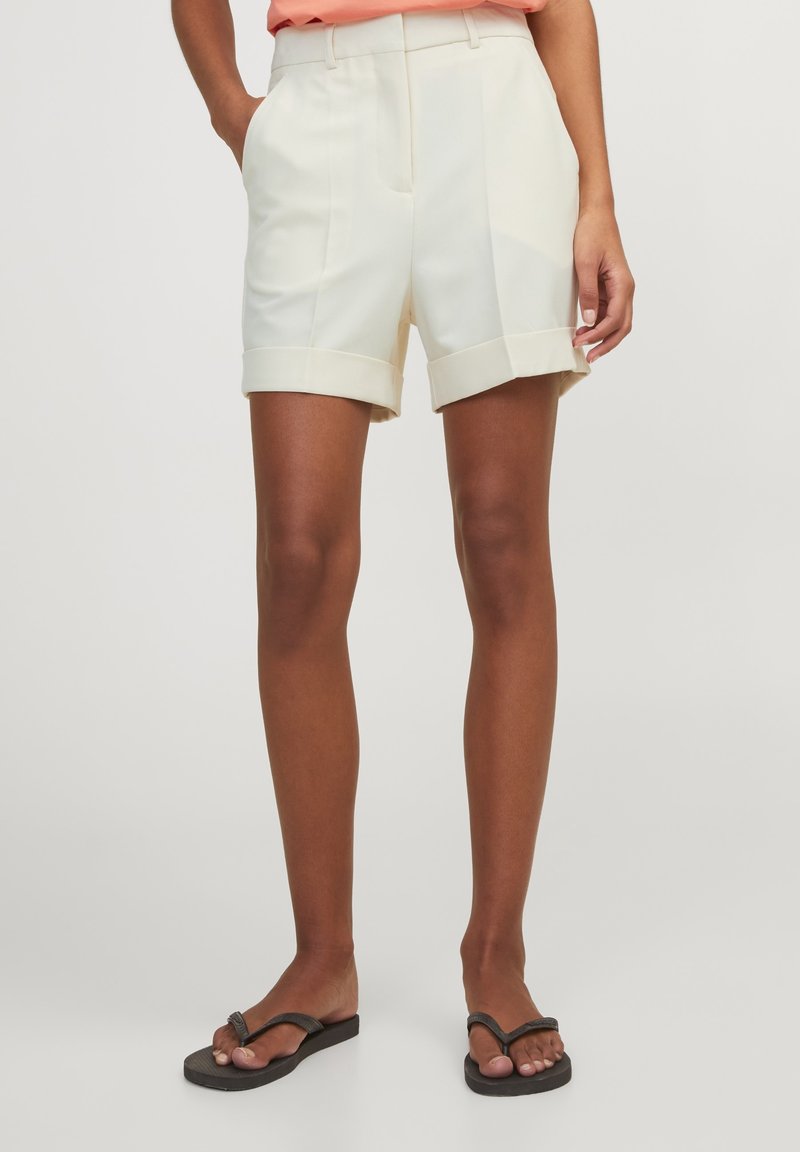 Krämfärgade skräddarsydda shorts med arbetad nederkant, två sidofickor och framveck. Tillverkade av ett slätt tyg med en lätt textur.