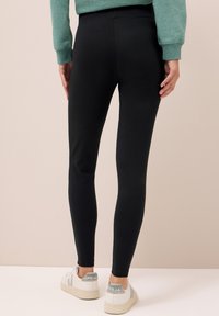 Leggings noirs en matériau extensible, design ajusté et texture lisse. Associés à des baskets blanches avec des accents gris.