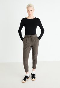 Maglietta nera a maniche lunghe, pantaloni a quadri marroni a vita alta con cordoncino e sneakers nere con dettagli bianchi e calzini.