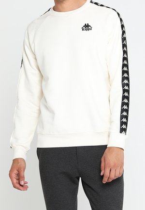 Cream-colored sweatshirt with black Kappa logo, ribbed neckline and cuffs, contrasting black side stripes featuring a repeated logo pattern.