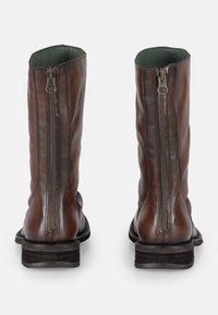 Bottes en cuir marron avec une finition texturée, dotées de deux zips latéraux et d'un talon empilé. L'intérieur est doublé de tissu vert.