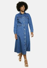 Denims krekls kleita ar garām piedurknēm, pogu aizdari, divām krūšu kabatām, sašaurinātu jostasvietu un pilnu svārku vidēji zilā mazgājumā.