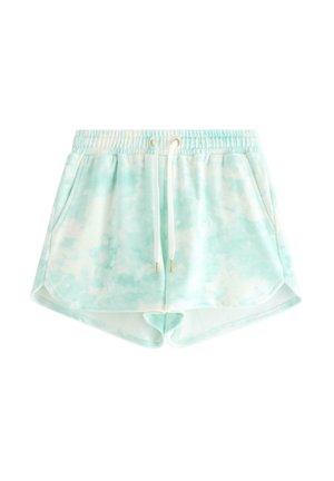Teenagepige står iført en lyseblå og hvid tie-dye hættetrøje med lynlås, matchende shorts, hvid trykt t-shirt og lysegrønne flip-flops.