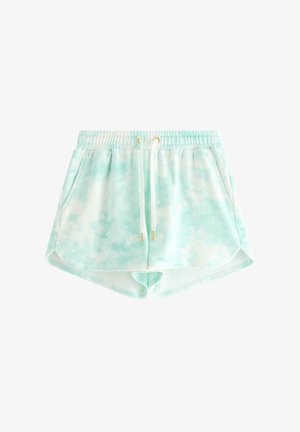 Teenagepige står iført en lyseblå og hvid tie-dye hættetrøje med lynlås, matchende shorts, hvid trykt t-shirt og lysegrønne flip-flops.