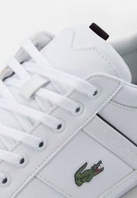 Gros plan sur une sneaker blanche Lacoste avec des lacets blancs, un logo crocodile vert brodé et des détails de panneaux cousus.