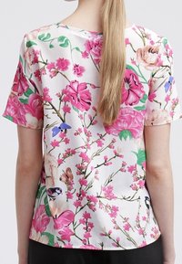 Kwiatowa bluzka z krótkim rękawem z jedwabistego materiału, z jasnym różowym i zielonym wzorem kwiatowym oraz akcentami w kolorze niebieskim i kremowym, o luźnym kroju.