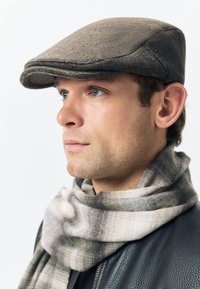 Gray flat cap made of wool, featuring a rounded crown and small brim. Wrapped in a plaid-patterned scarf in neutral tones.