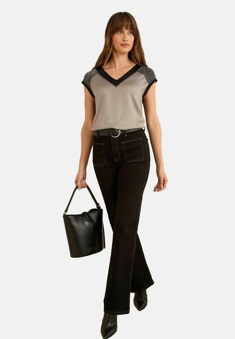 Top gri cu mâneci scurte, cu borduri negre și umeri decorativi, purtat cu pantaloni negri evazați și o geantă neagră. Textură netedă, design modern.