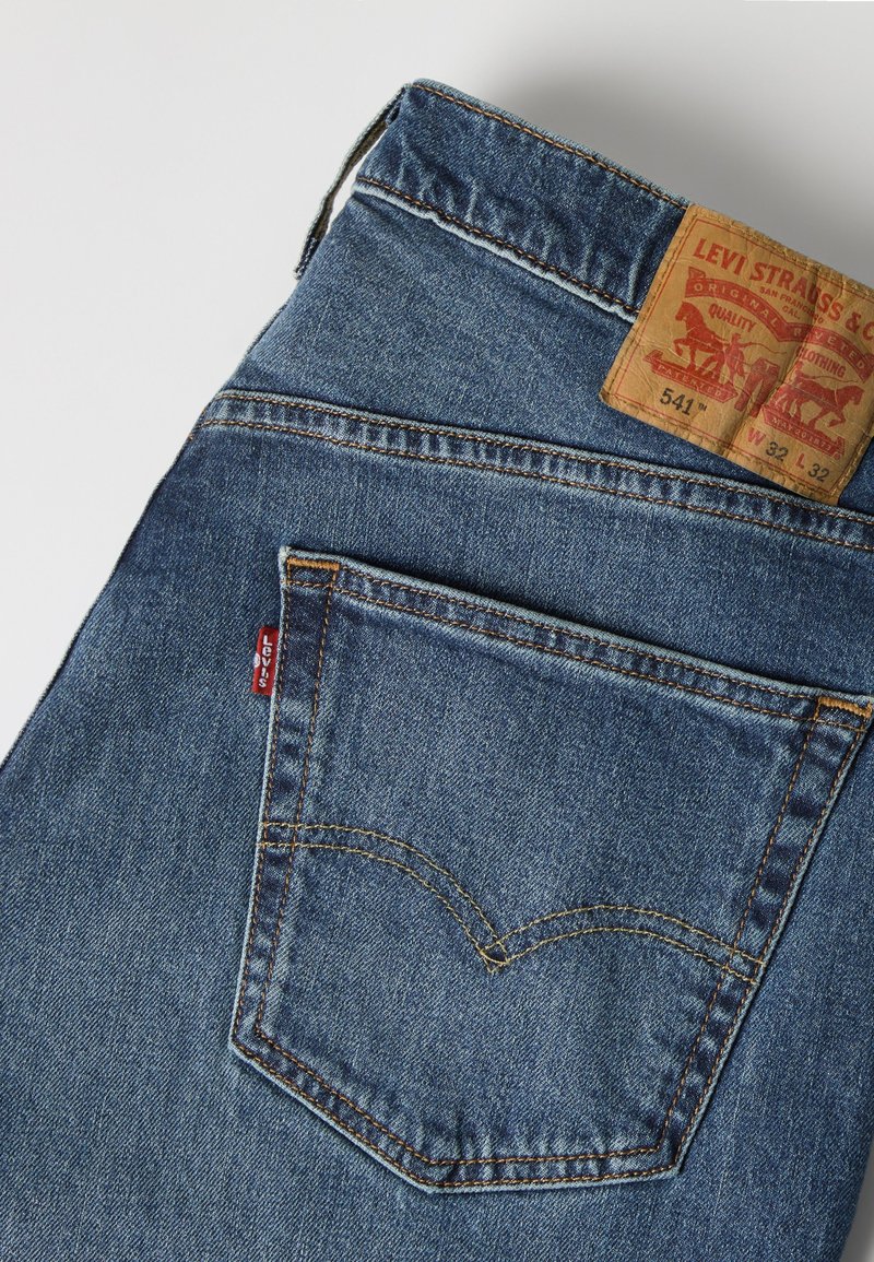 Blue Levi's denim jeans folded showing back pocket with stitching, red Levi's tag, and leather brand patch with size details.