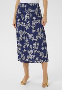 Jupe midi florale bleu marine avec une taille smockée, ornée de motifs de feuilles blanches. Tissu léger avec une texture fluide.